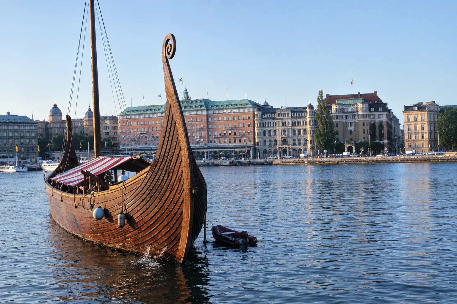 Replica Viking longship moored on the water in central Stockholm, with the city's waterfront and Swedish flags behind it on a summer evening