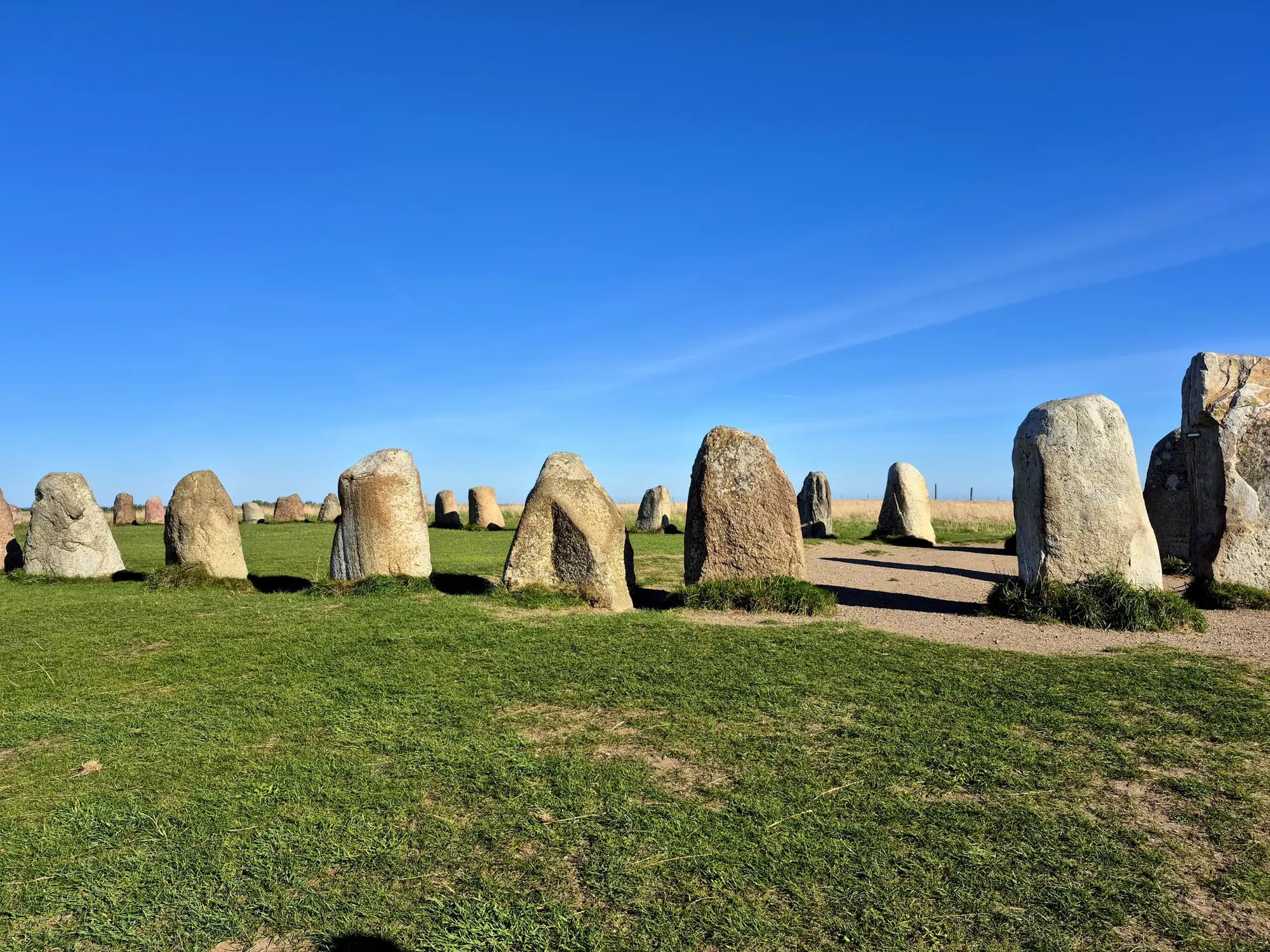 A curving line of tall standing stones on green grass under a deep blue sky, part of the stone ship of Ales stenar above Kåseberga in Skåne
