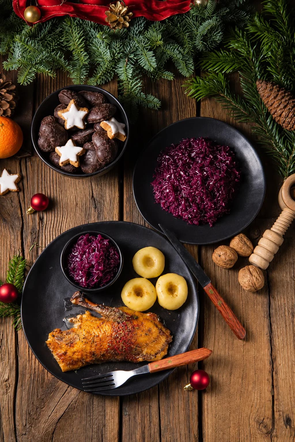 Roast goose leg with red cabbage and potato dumplings on a dark plate, on a rustic wooden table with fir branches