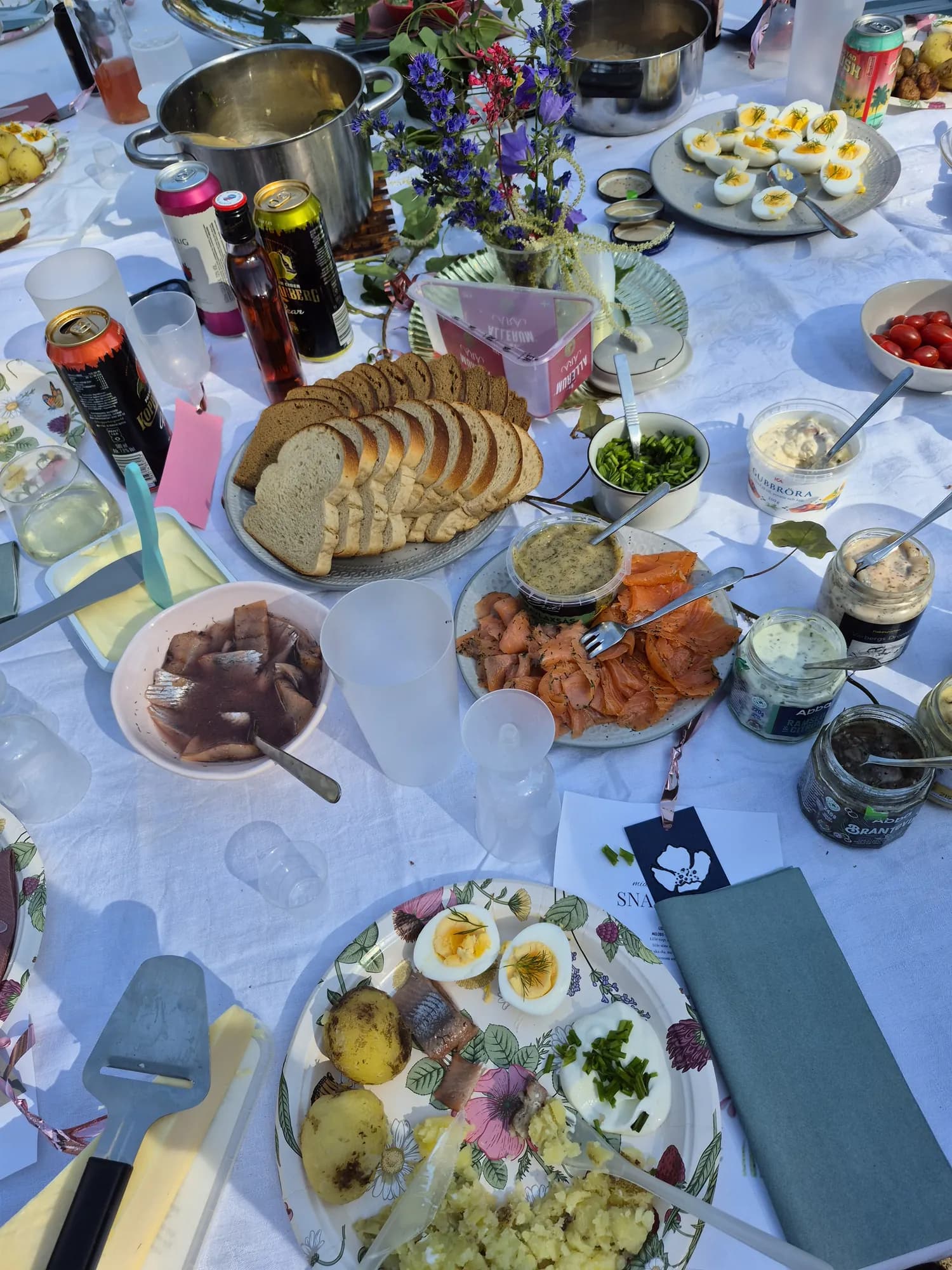 A Midsummer Eve table in Skåne seen from above: pickled herring, smoked salmon, boiled eggs, new potatoes with dill, bread and sauces on a white cloth
