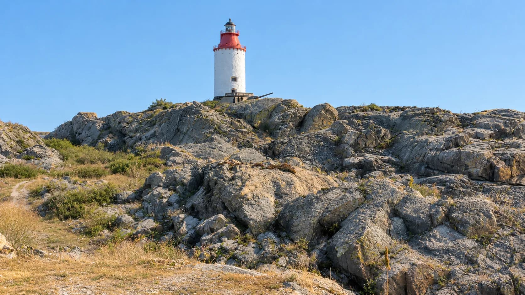 White stone lighthouse with a red top on a ridge of bare grey rock under a clear blue sky at Landsort, on Öja in the southern Stockholm archipelago