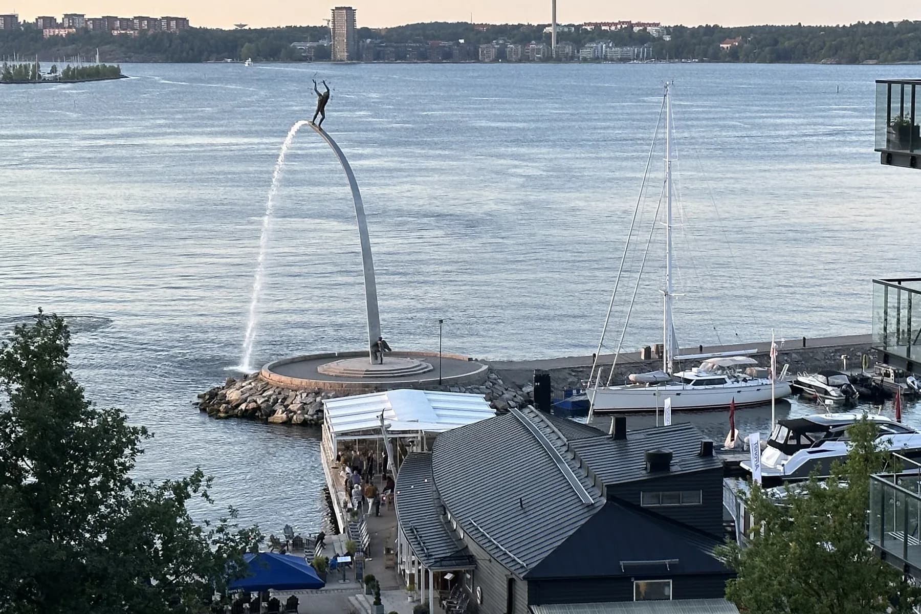 The pier at Nacka Strand seen from above, with Carl Milles's arched fountain sculpture at its end, a sailing boat moored alongside and open water beyond
